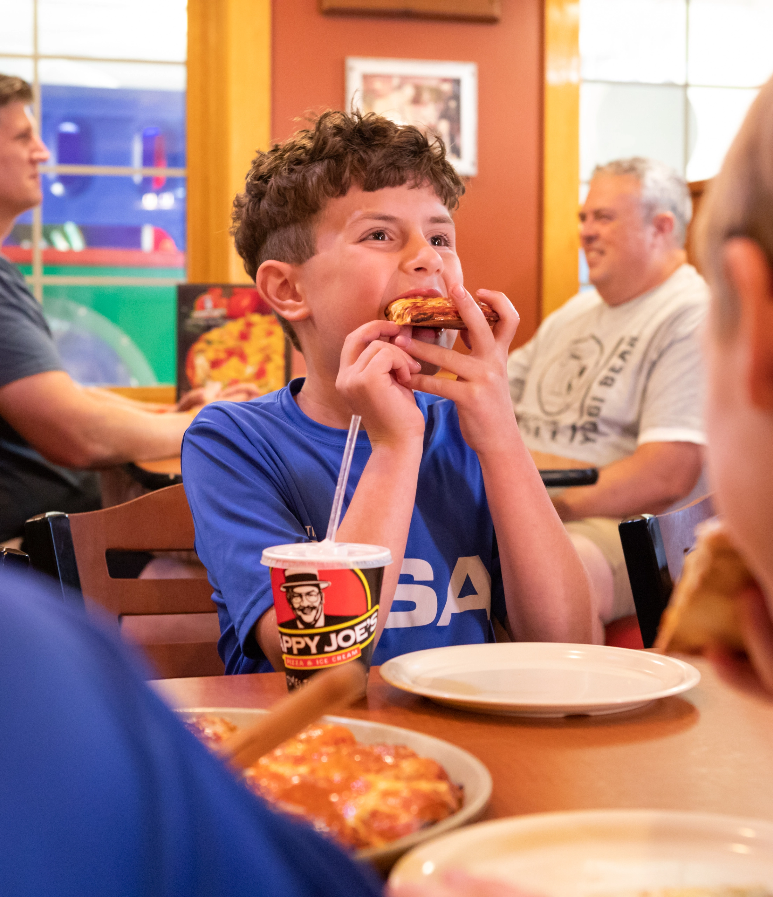 Boy eating a slice of Happy Joe;s Pizza.
