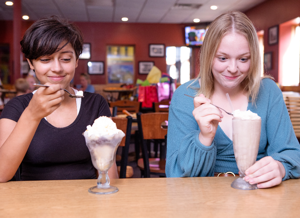 Two women eating a sundae and milk shake.