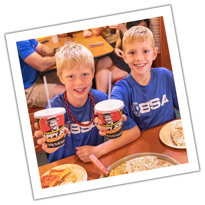 Boys holding up Happy Joe's cups next to pizzas.